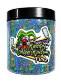 A clear plastic jar filled with holographic glitter in blue, green, purple, and orange tones, with a black lid. A large sticker on the front shows a clown and the text 'Kandy Coated Kustoms Flake'.